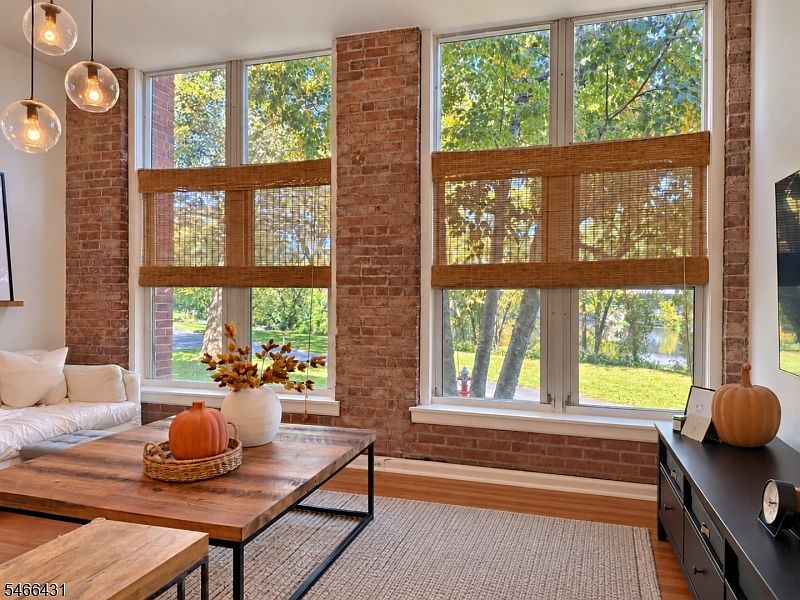 Living room with exposed brick, tall windows, and river views at The Mill in Little Falls